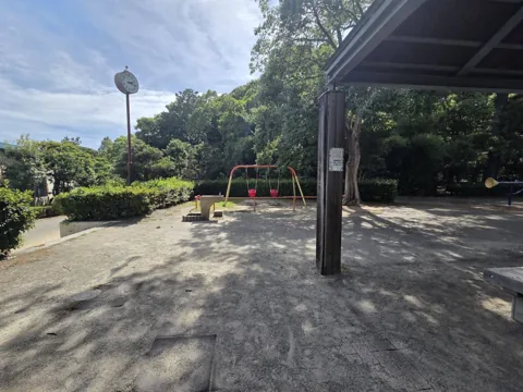 かぶと塚公園：東屋の下から見た遊具広場（ブランコ・時計塔）