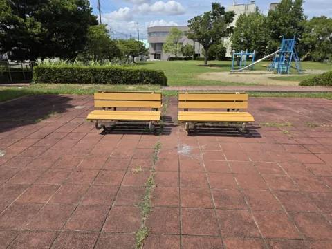 北川瀬公園：ベンチ2脚（タイル敷き広場）。奥に複合遊具