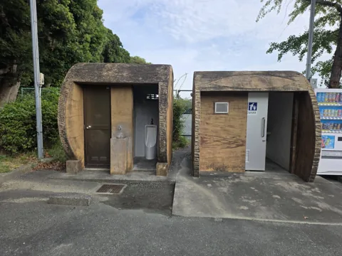 中央公園：トイレ外観（丸太風デザイン）。多目的トイレの表示、隣に自動販売機