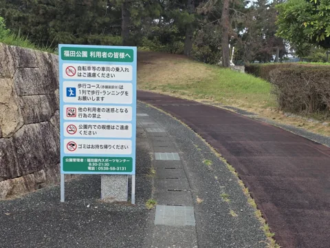 福田公園：赤舗装の歩行コース脇に立つ公園利用案内